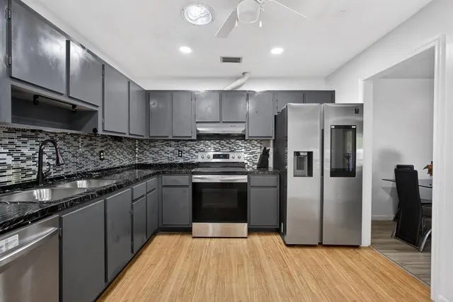 a kitchen with stainless steel appliances granite countertop a refrigerator a sink dishwasher a stove with wooden floors and cabinets