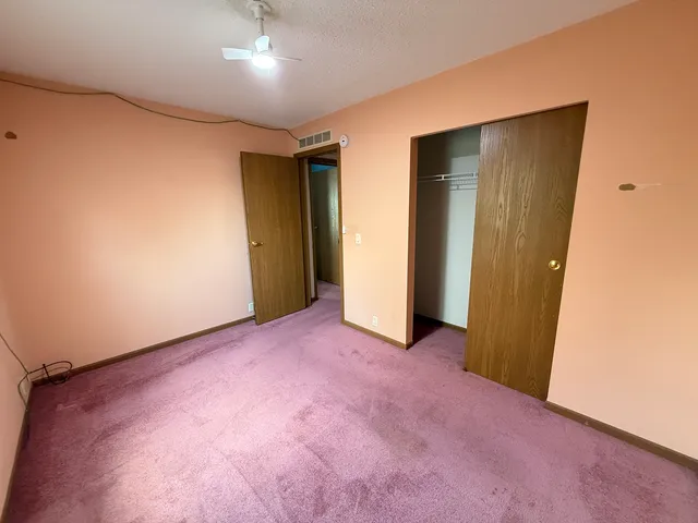 an empty room with chandelier fan and windows