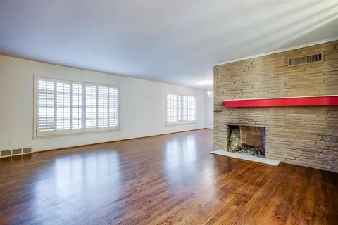 an empty room with wooden floor fireplace and windows