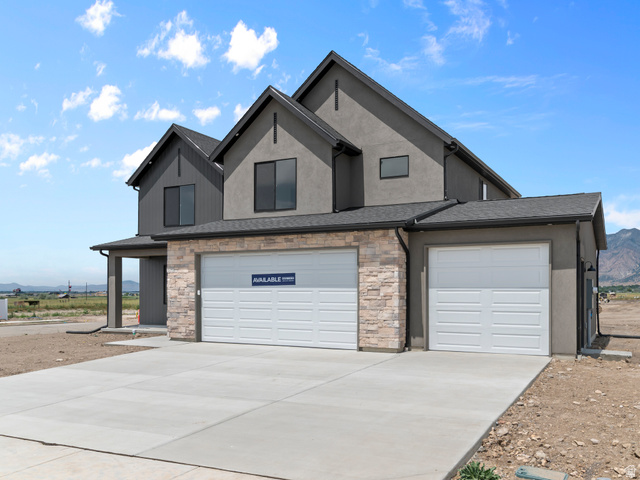 1380 West 2350 South, Unit 16 Perry, UT 84302 - Photo 1 of 34 Modern exterior featuring a stucco and stone facade, contrasting dark siding accents, and a multi-car garage with concrete driveway