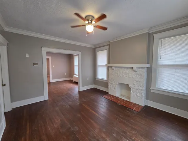an empty room with wooden floor a ceiling fan a fireplace and windows