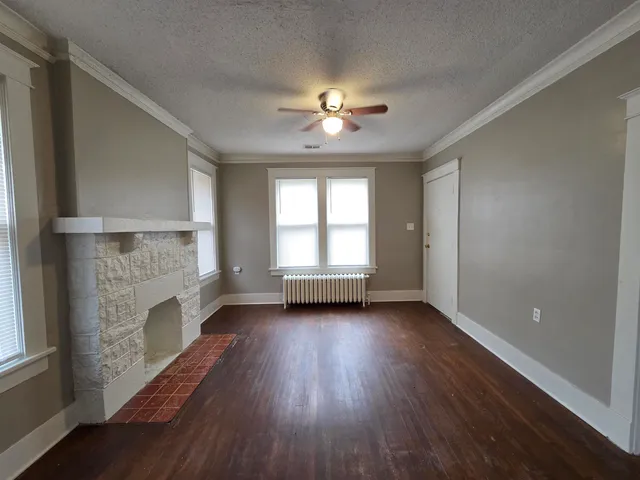 an empty room with wooden floor fireplace and windows