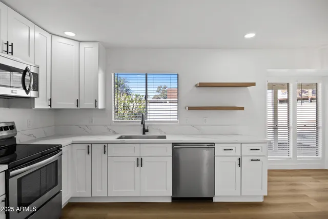 a kitchen with stainless steel appliances granite countertop a sink a stove a refrigerator and white cabinets