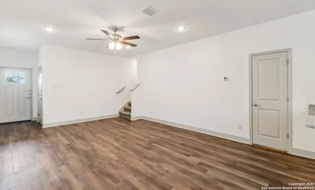 a view of an empty room with wooden floor and a ceiling fan