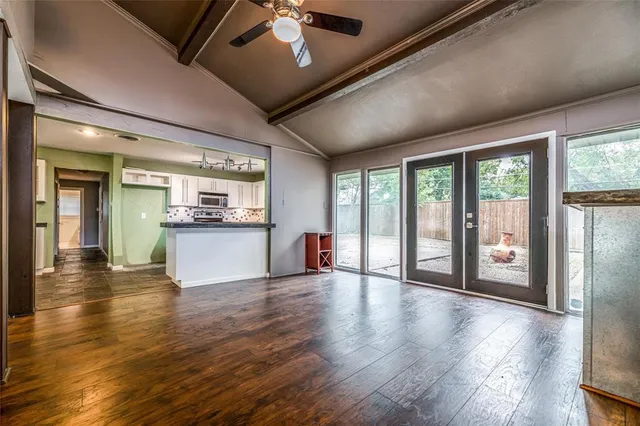 a view of an empty room with wooden floor and a kitchen