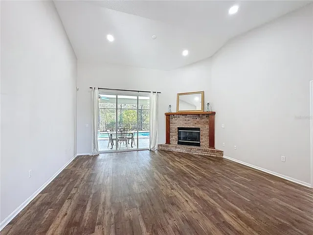 a view of an empty room with wooden floor fireplace and a window