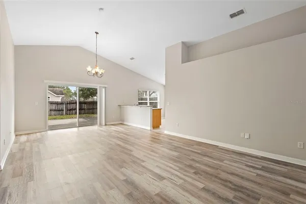 a view of an empty room with wooden floor kitchen view and a window