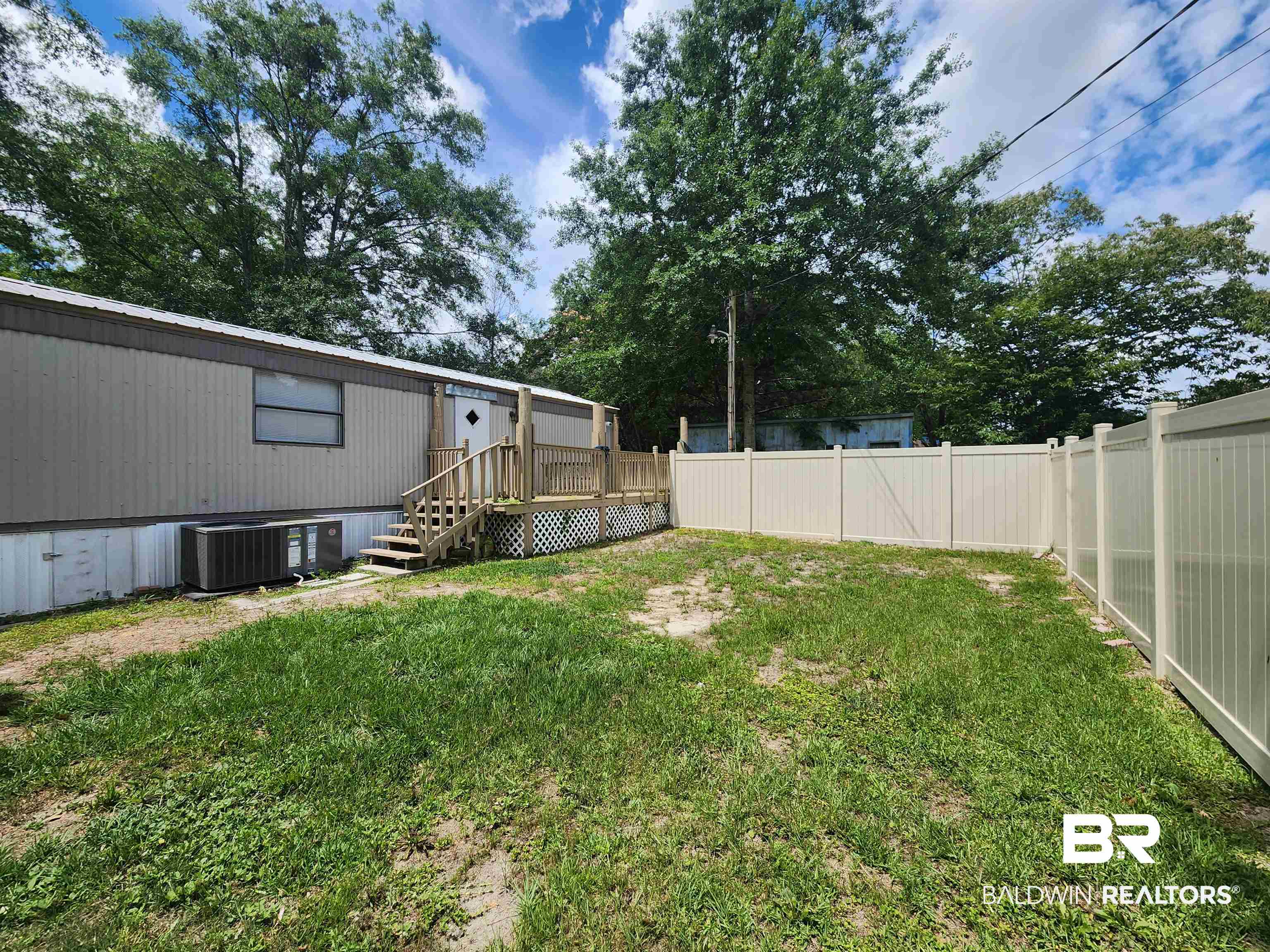 23051 Fritz Lane Foley, AL 36535 - Photo 5 of 26 Spacious outdoor area featuring a light-colored privacy fence, a wooden deck with lattice skirting, and mature perimeter trees
