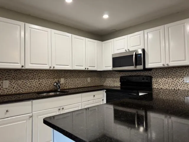 a kitchen with stainless steel appliances granite countertop a refrigerator a sink a stove a microwave and white cabinets