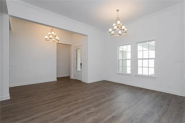 an empty room with wooden floor chandelier and window