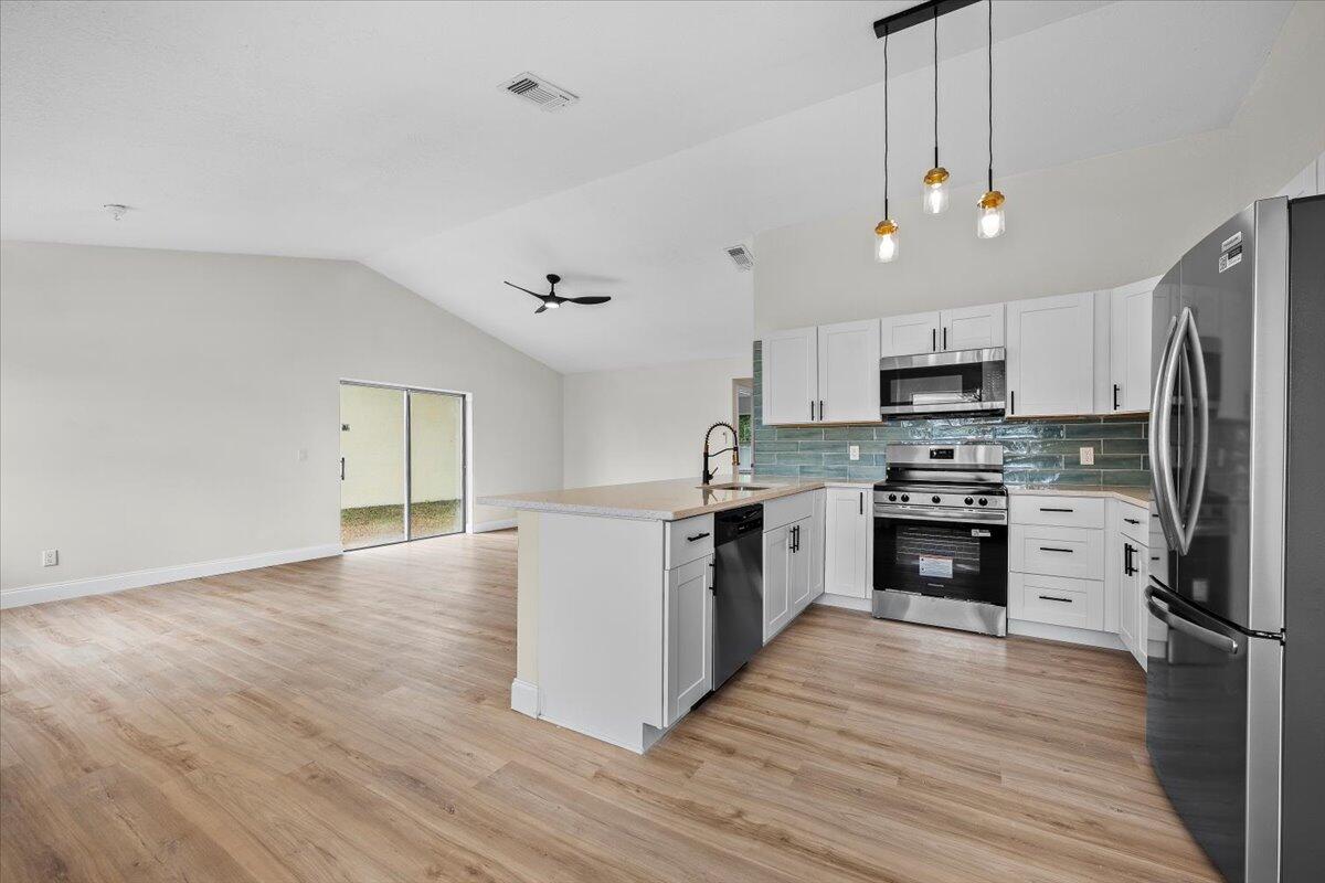 126 Wandering Trail Jupiter, FL 33458 - Photo 6 of 16 a kitchen with granite countertop a refrigerator a stove top oven a sink dishwasher a refrigerator and white cabinets with wooden floor