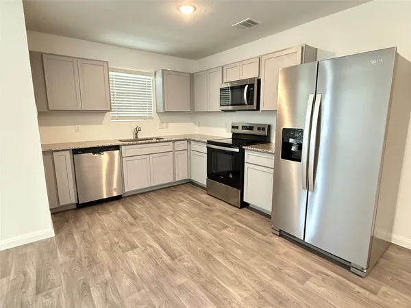 a kitchen with granite countertop stainless steel appliances a refrigerator a stove top oven and white cabinets