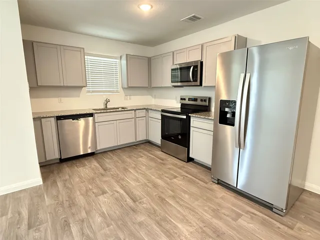 a kitchen with granite countertop stainless steel appliances a refrigerator a stove top oven and white cabinets