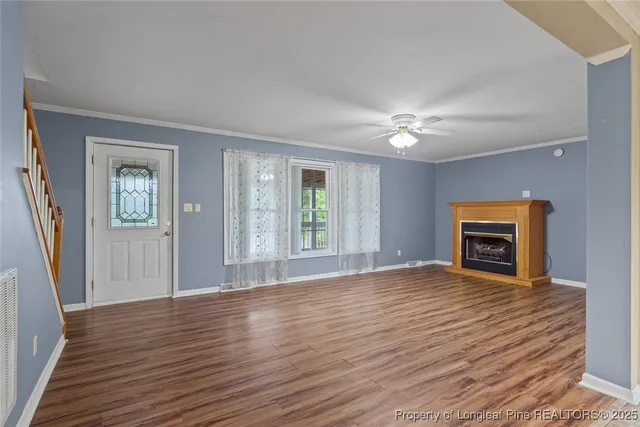 a view of an empty room with wooden floor fireplace and a window