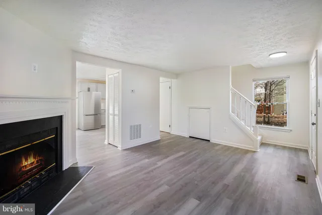 a view of an empty room with wooden floor fireplace and a window