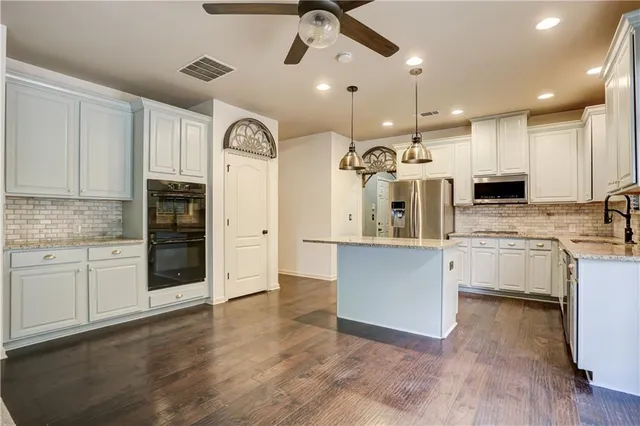 a kitchen with stainless steel appliances kitchen island granite countertop a stove a sink and white cabinets with wooden floor