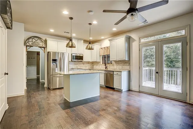 a large kitchen with stainless steel appliances kitchen island granite countertop a stove a refrigerator a sink and white cabinets with wooden floor