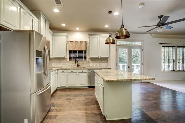 a kitchen with stainless steel appliances kitchen island granite countertop a refrigerator a sink dishwasher a stove and white cabinets with wooden floor