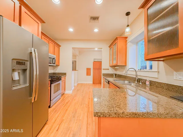 a kitchen with stainless steel appliances granite countertop a refrigerator a stove and a sink with wooden floor