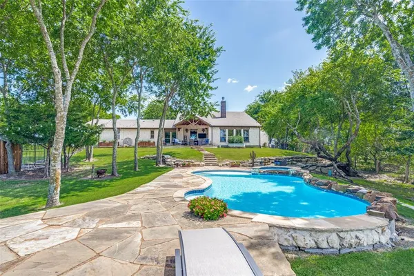 a view of swimming pool with lawn chairs and large trees