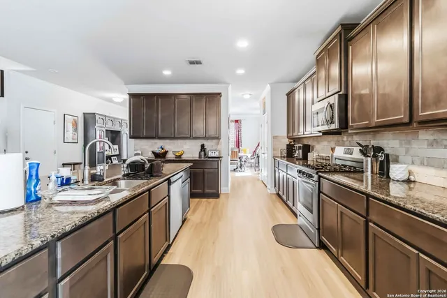 a large kitchen with granite countertop lots of counter top space a sink and stainless steel appliances