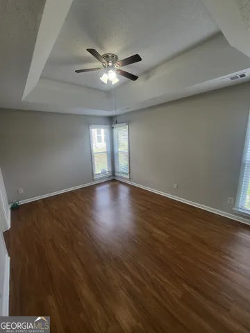 a view of an empty room with wooden floor and a fan