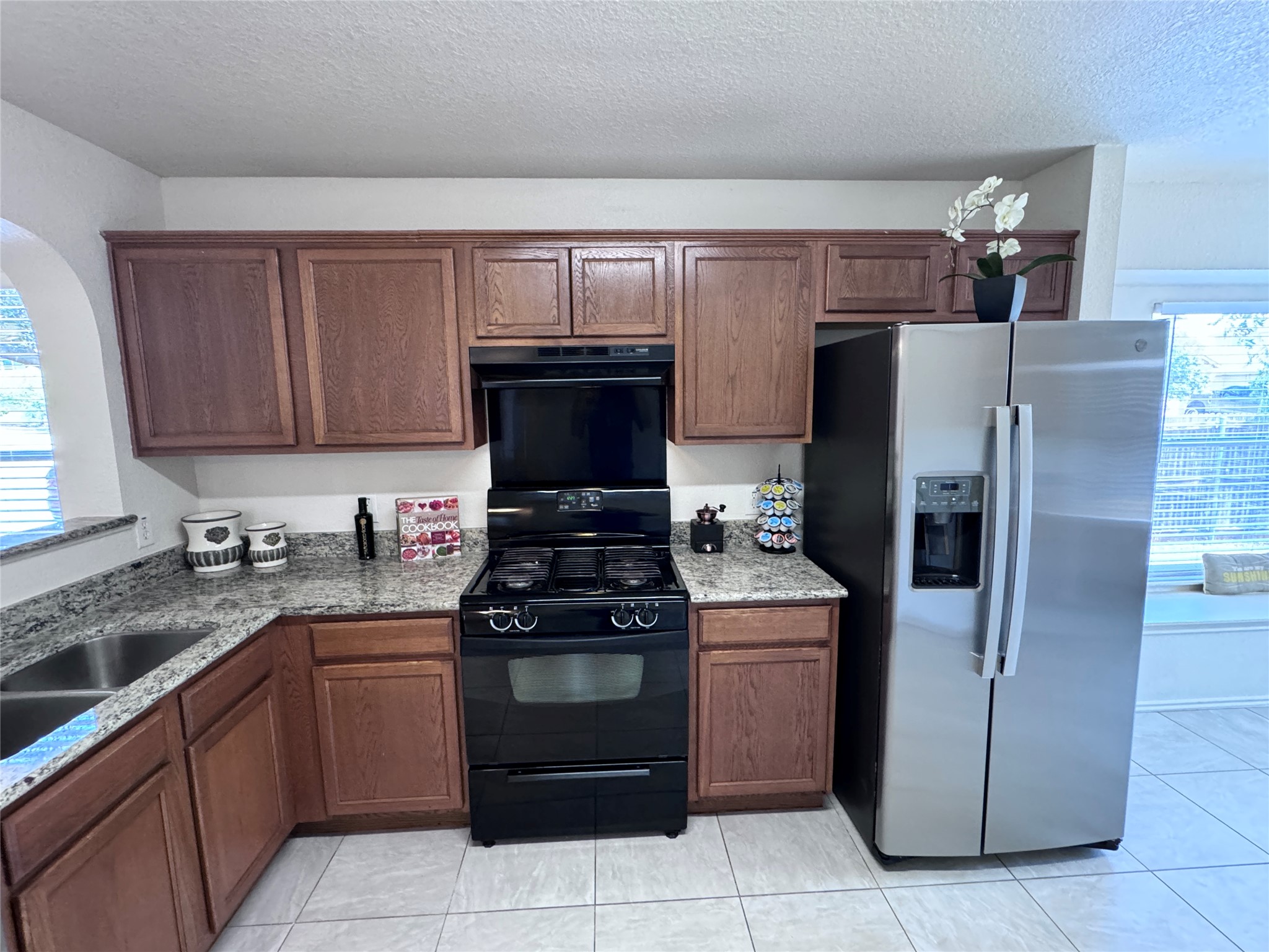 3411 Wickham Lane Austin, TX 78725 - Photo 4 of 20 Kitchen featuring black range with gas stovetop, stainless steel fridge with ice dispenser, light granite counters, and wood finish cabinets