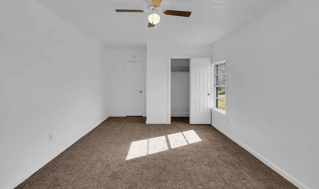an empty room with chandelier fan and windows