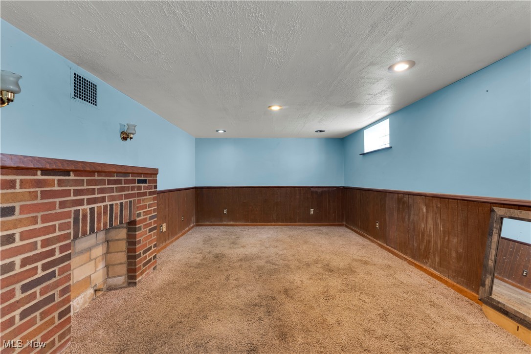 3739 Warren Road Cleveland, OH 44111 - Photo 10 of 40 Below grade area featuring a textured ceiling, carpet flooring, a brick fireplace, wainscoting, and wooden walls