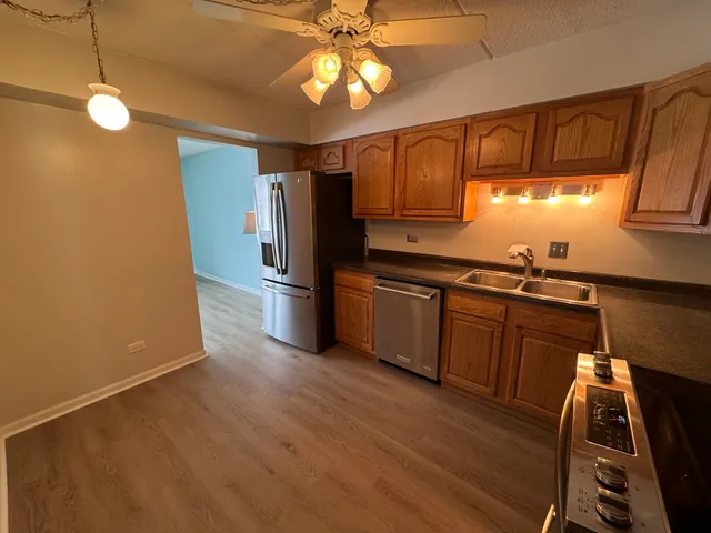 a kitchen with stainless steel appliances granite countertop a refrigerator a sink dishwasher a dining table and chairs with wooden floor