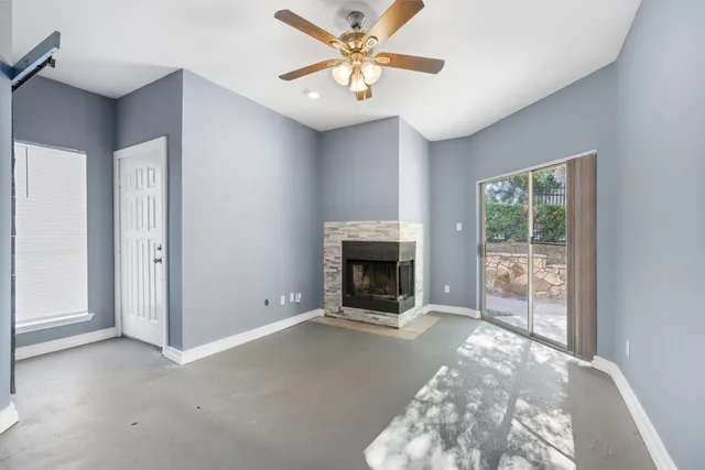 a view of a livingroom with a fireplace a ceiling fan and windows