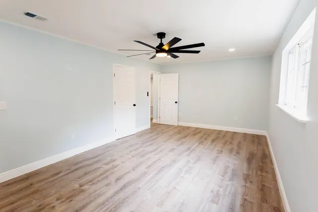 an empty room with wooden floor fan and windows