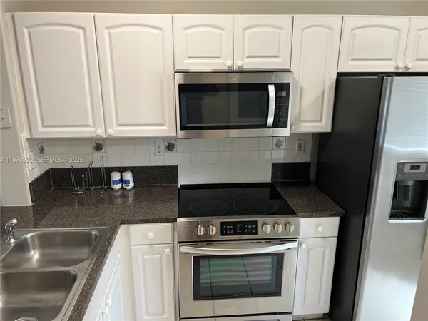 a kitchen with stainless steel appliances granite countertop white cabinets a stove a microwave and a sink