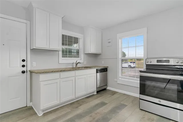 a kitchen with granite countertop white cabinets stainless steel appliances a sink and a window