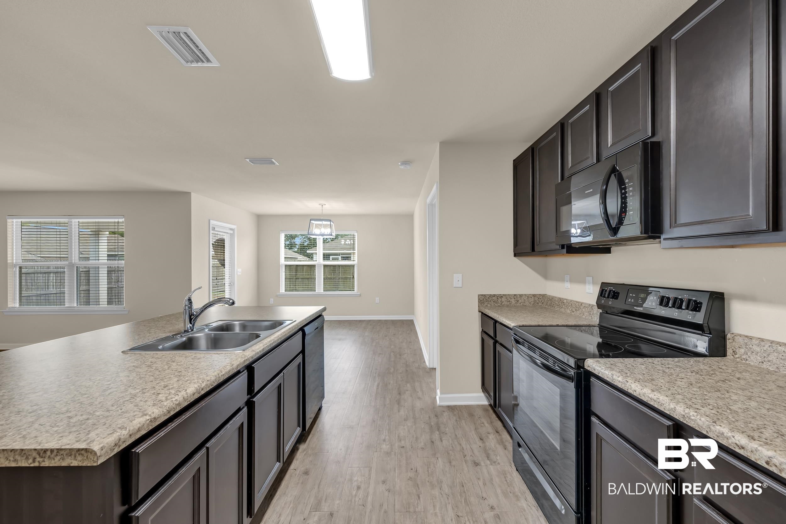 17344 Harding Drive Foley, AL 36535 - Photo 8 of 46 Kitchen featuring dark wood-finish cabinetry, speckled countertops, stainless steel double basin sink, and black appliances including a range and built-in microwave