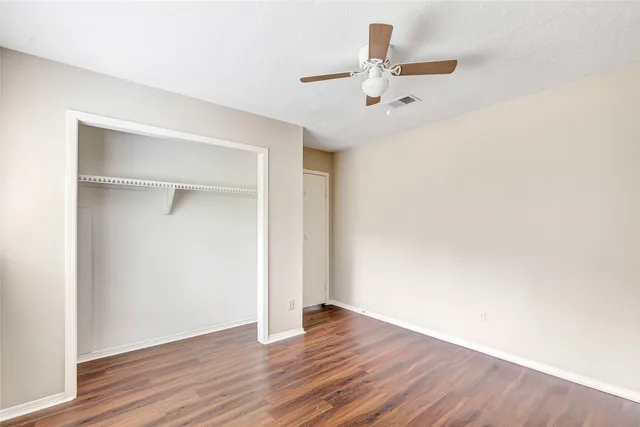 an empty room with wooden floor fan and windows