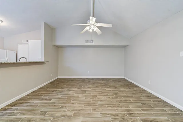 a view of an empty room with chandelier fan and wooden floor