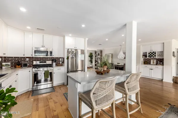 a kitchen with stainless steel appliances kitchen island granite countertop a refrigerator a stove a sink a dining table and chairs with wooden floor