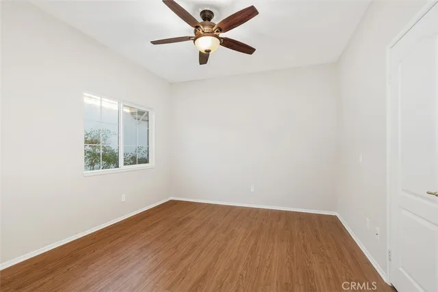 an empty room with wooden floor ceiling fan and window