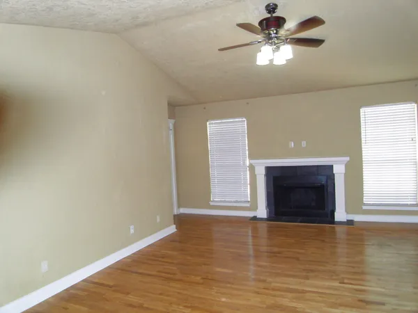an empty room with wooden floor fireplace and fan