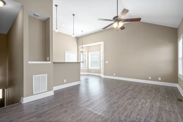 a view of an empty room with wooden floor and a ceiling fan