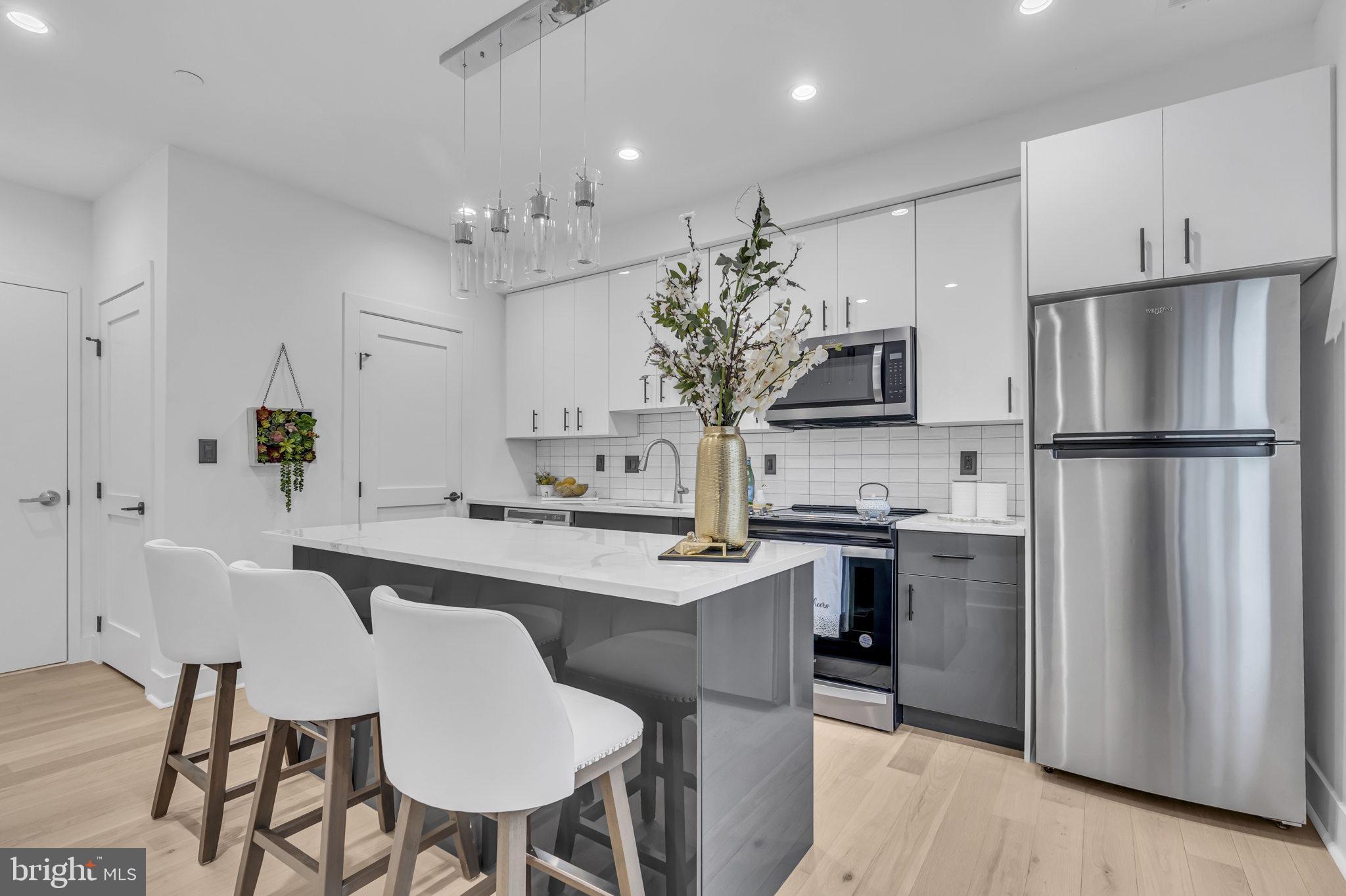 1103 Fern Street Northwest, Unit 301 Washington, DC 20012 - Photo 25 of 57 a kitchen with stainless steel appliances a dining table chairs refrigerator and microwave