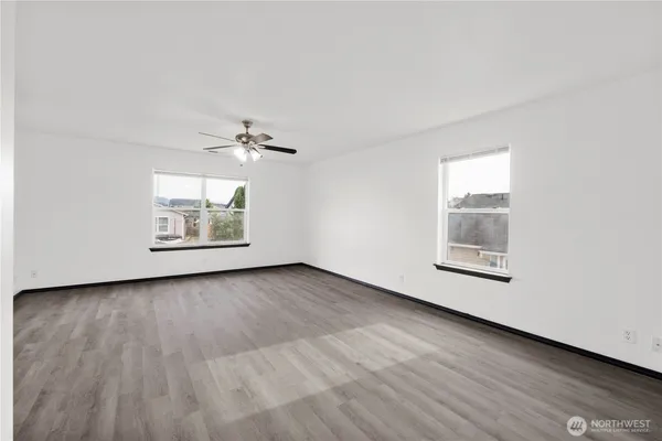 an empty room with wooden floor a ceiling fan and windows