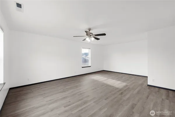 an empty room with wooden floor chandelier fan and windows