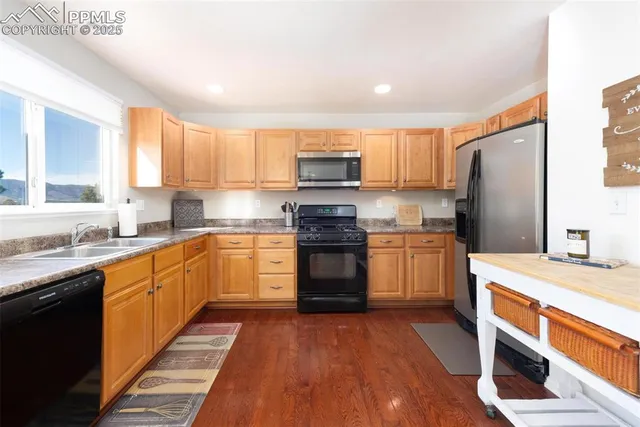 a kitchen with granite countertop wooden floors stainless steel appliances a sink and a window