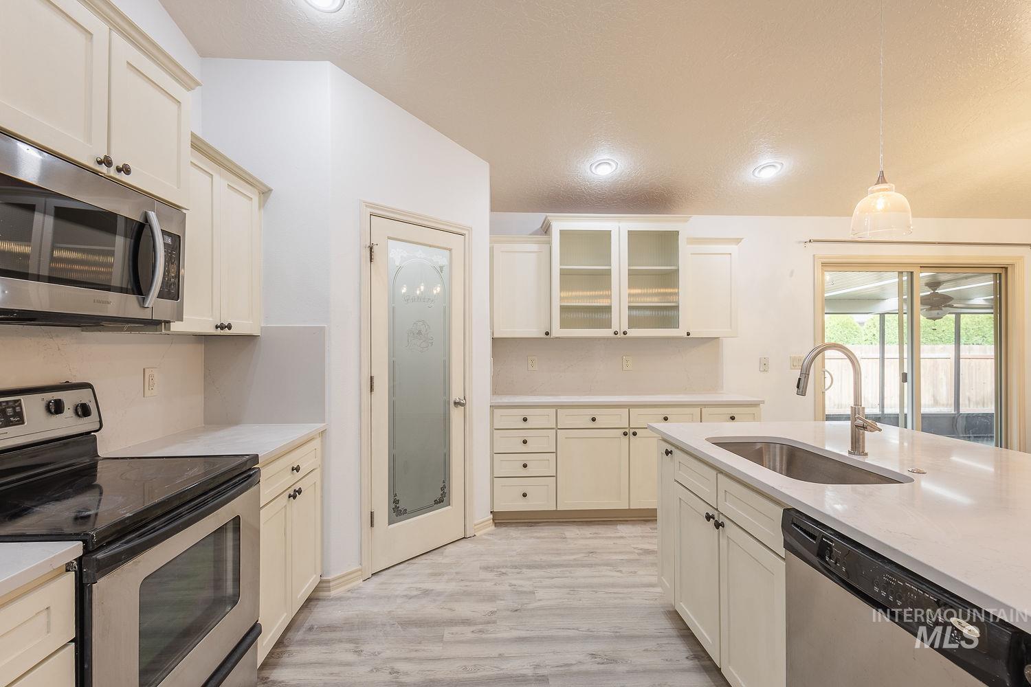 4227 North Rhodes Avenue Meridian, ID 83646 - Photo 13 of 42 Kitchen featuring stainless steel appliances, glass fronted cabinets, a textured ceiling, hanging light fixtures, and light wood-style floors