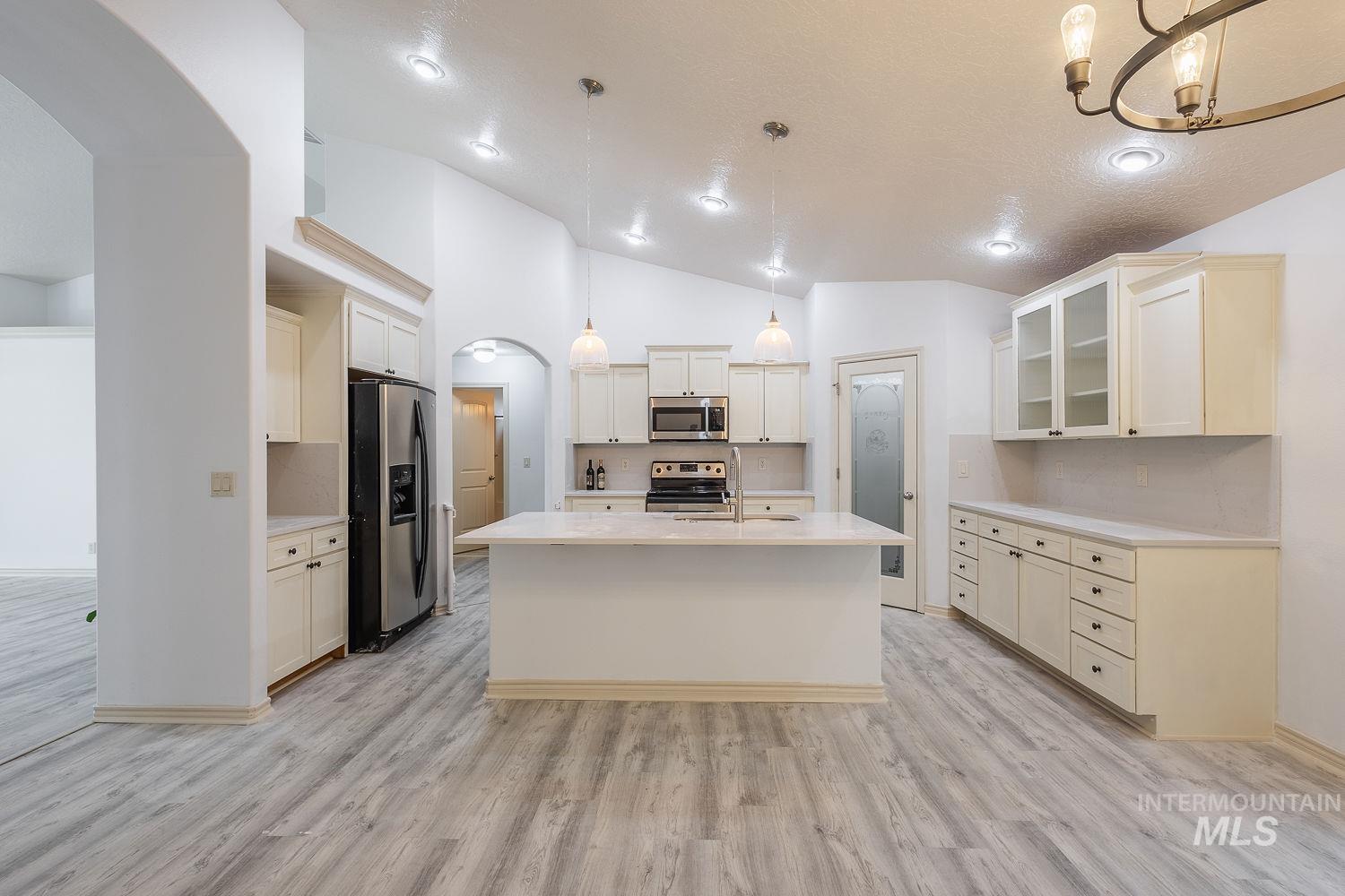 4227 North Rhodes Avenue Meridian, ID 83646 - Photo 17 of 42 Kitchen with decorative backsplash, arched walkways, lofted ceiling, stainless steel appliances, and glass fronted cabinets