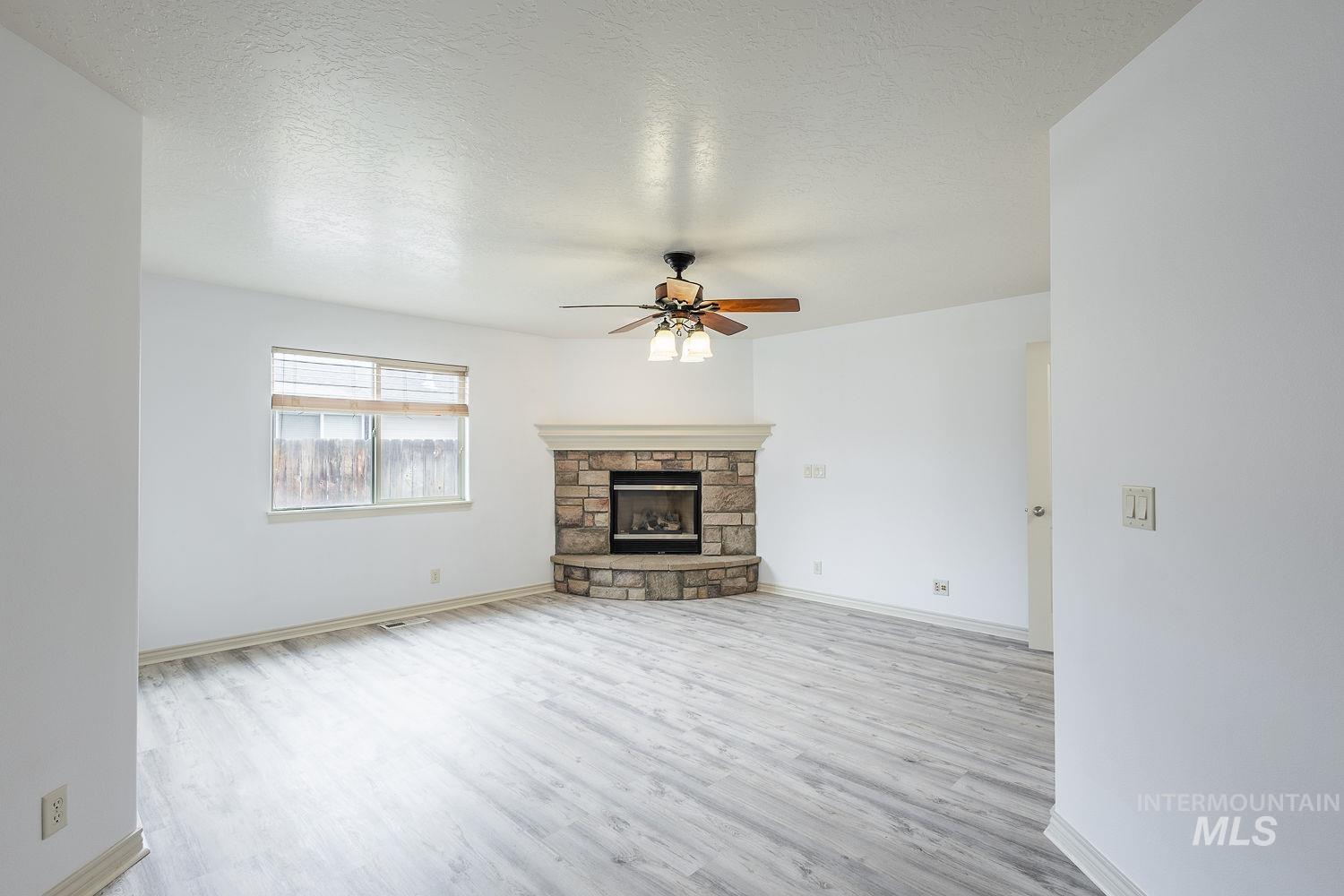 4227 North Rhodes Avenue Meridian, ID 83646 - Photo 25 of 42 Unfurnished living room featuring a ceiling fan, a textured ceiling, a fireplace, and light wood finished floors