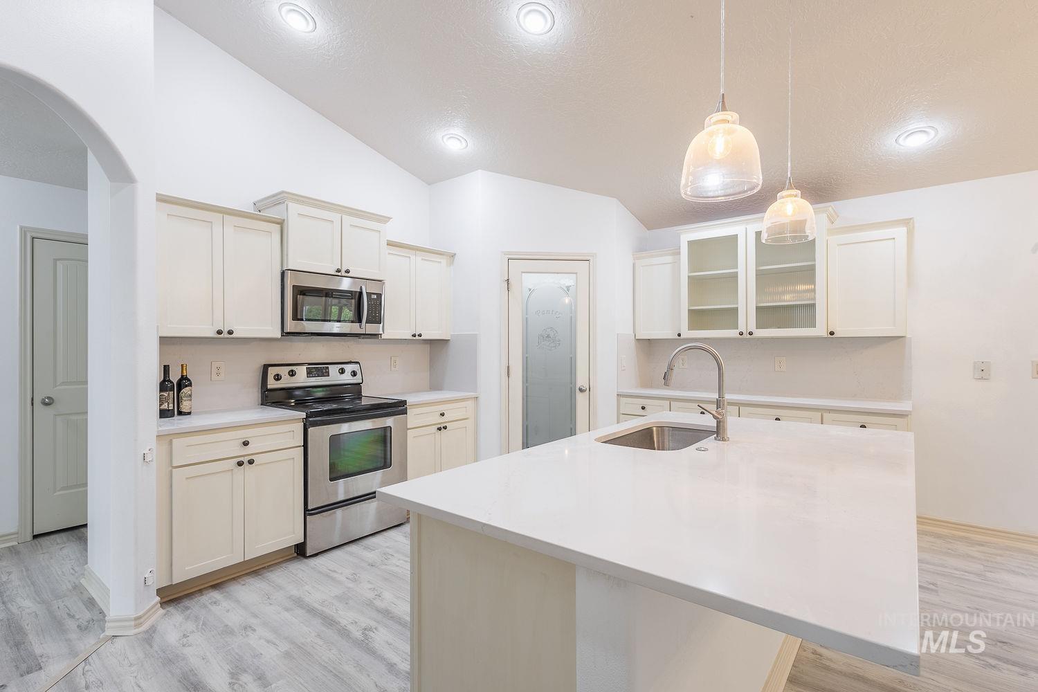 4227 North Rhodes Avenue Meridian, ID 83646 - Photo 7 of 42 Kitchen with stainless steel appliances, glass insert cabinets, a kitchen island with sink, arched walkways, and light wood-style floors