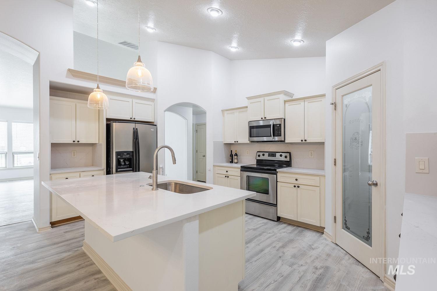 4227 North Rhodes Avenue Meridian, ID 83646 - Photo 8 of 42 Kitchen featuring stainless steel appliances, arched walkways, a kitchen island with sink, light wood finished floors, and decorative backsplash